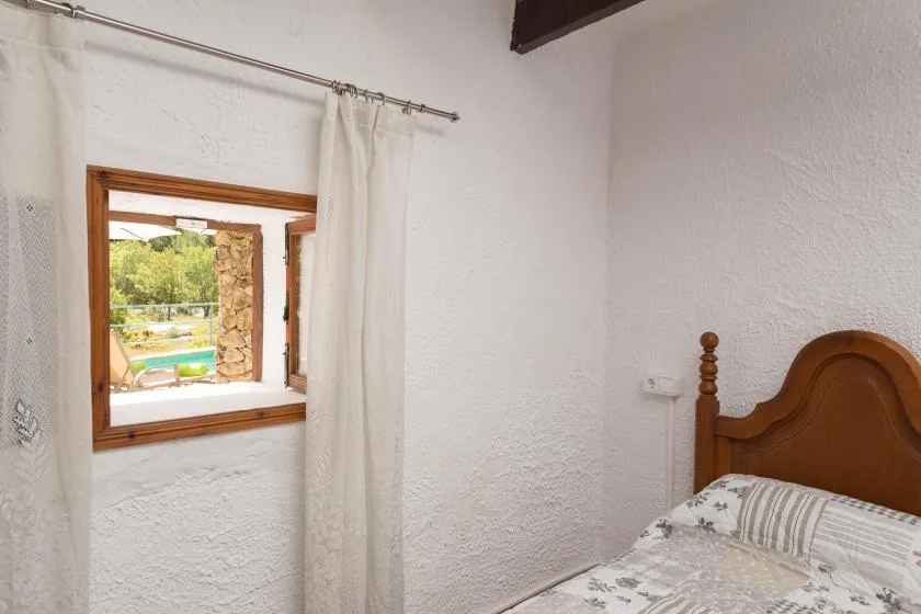 A bedroom with a wooden bed and a curtained window overlooking greenery.