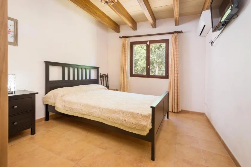 A bedroom with a bed, a window, and exposed ceiling beams.