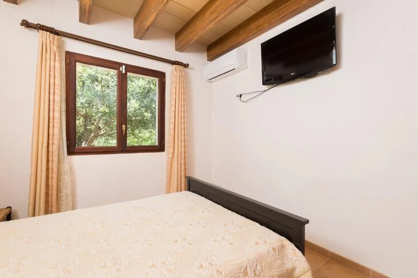 A bedroom with a bed, a curtained window, and a wall-mounted television.
