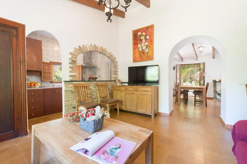 A bright living and dining area with a wooden table and arched openings.