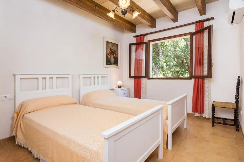 A bedroom with two single beds and a window overlooking greenery.