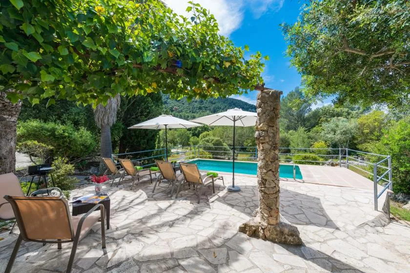 A shaded outdoor pool patio has seating and umbrellas beside the water.