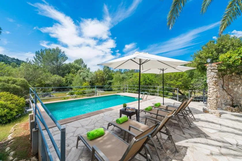 An outdoor poolside patio has lounge seating beneath a large umbrella.