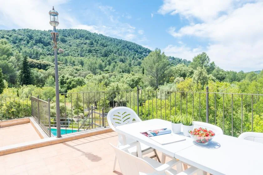 An outdoor dining area overlooks a green hillside, with a white table and chairs.