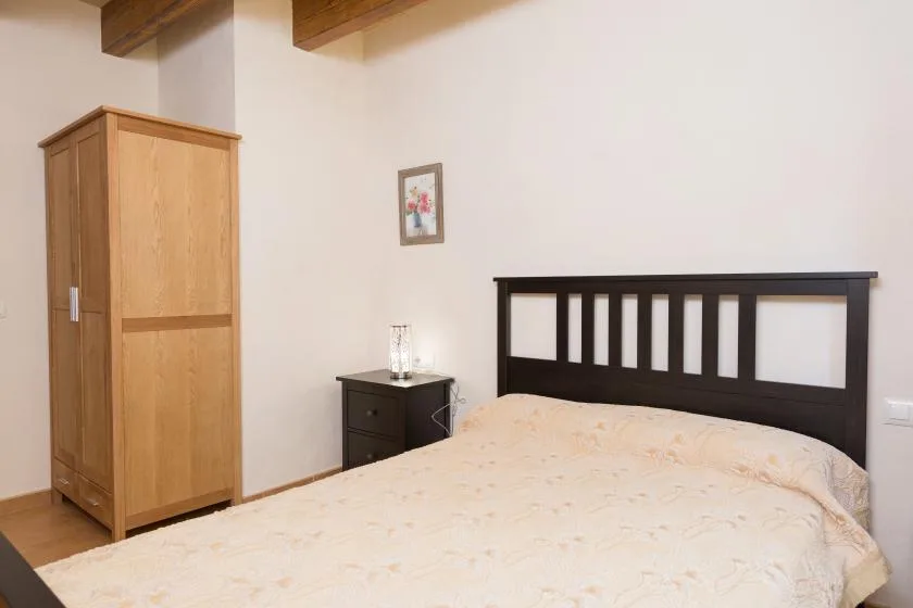 A bedroom with a bed, a wooden wardrobe, and a bedside table.