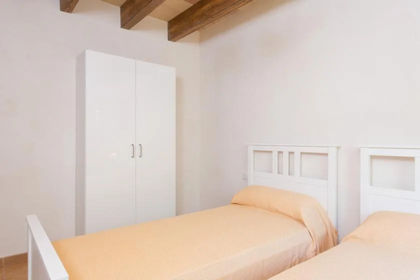 A bright bedroom with two beds and a white wardrobe.