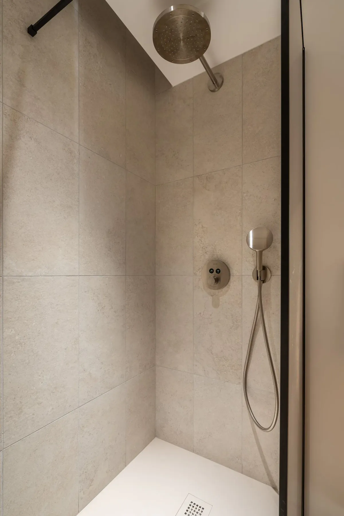 Una ducha revestida de azulejos con una ducha de mano y una ducha superior.
