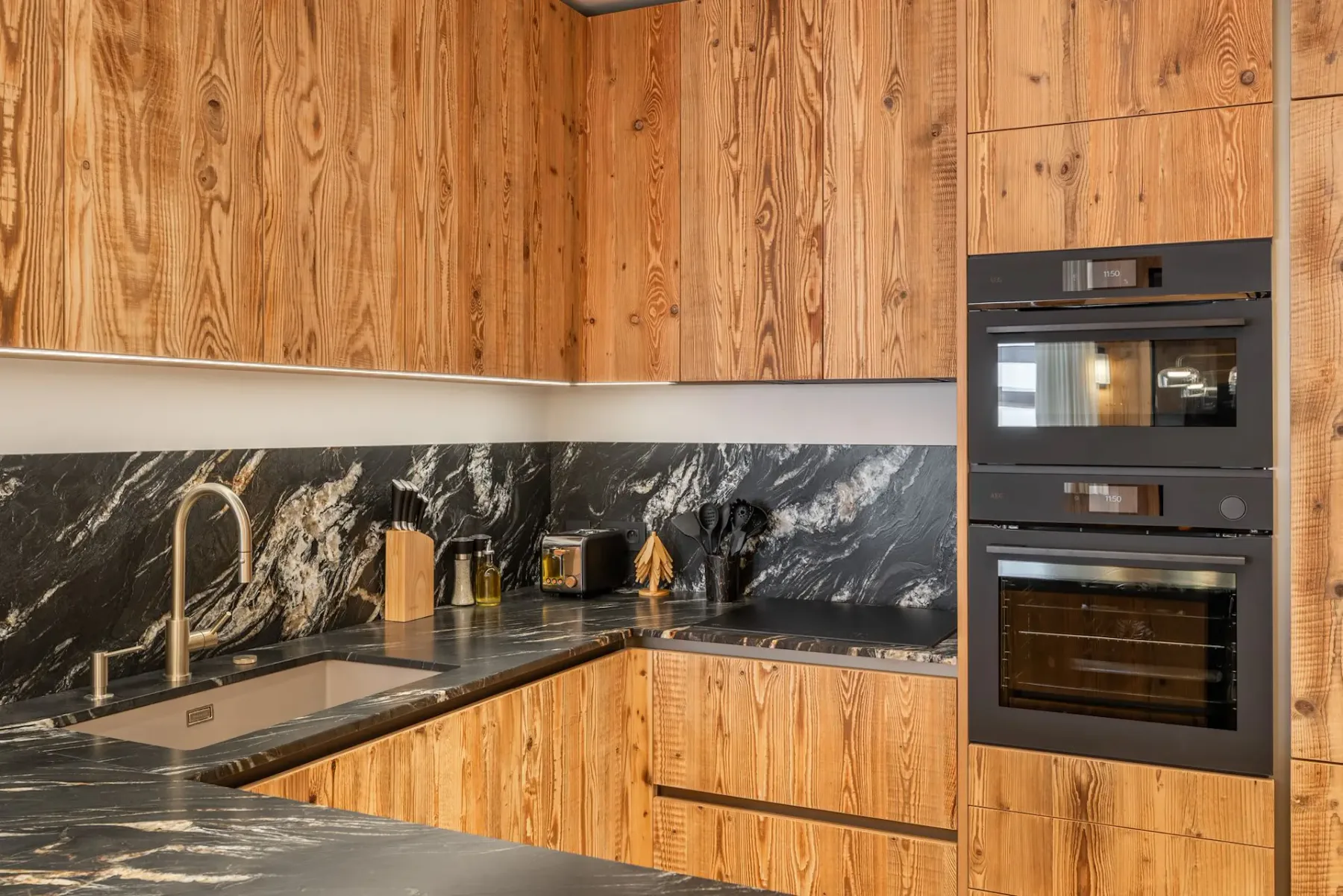 Una cocina con armarios de madera, encimeras oscuras y hornos empotrados.