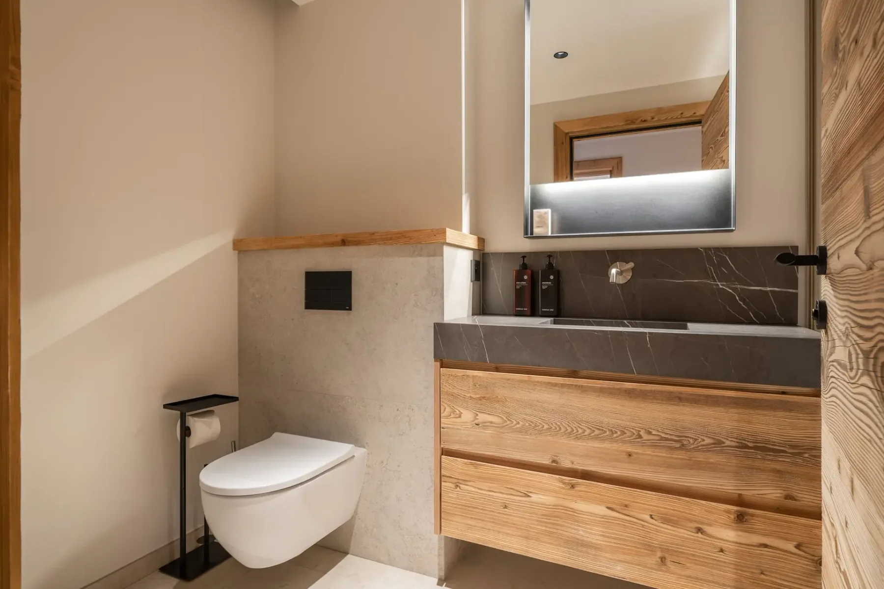 Baño moderno con mueble de madera, encimera gris y espejo iluminado.