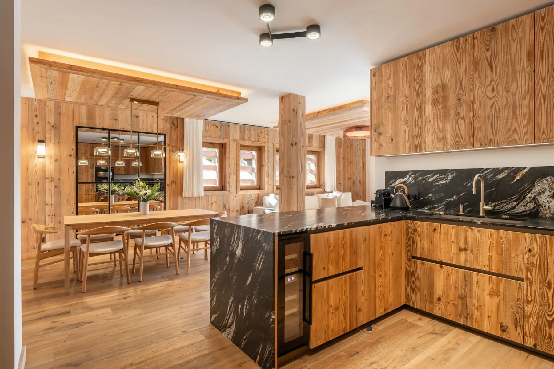 Cocina revestida de madera con una isla oscura y una mesa de comedor en el área contigua.