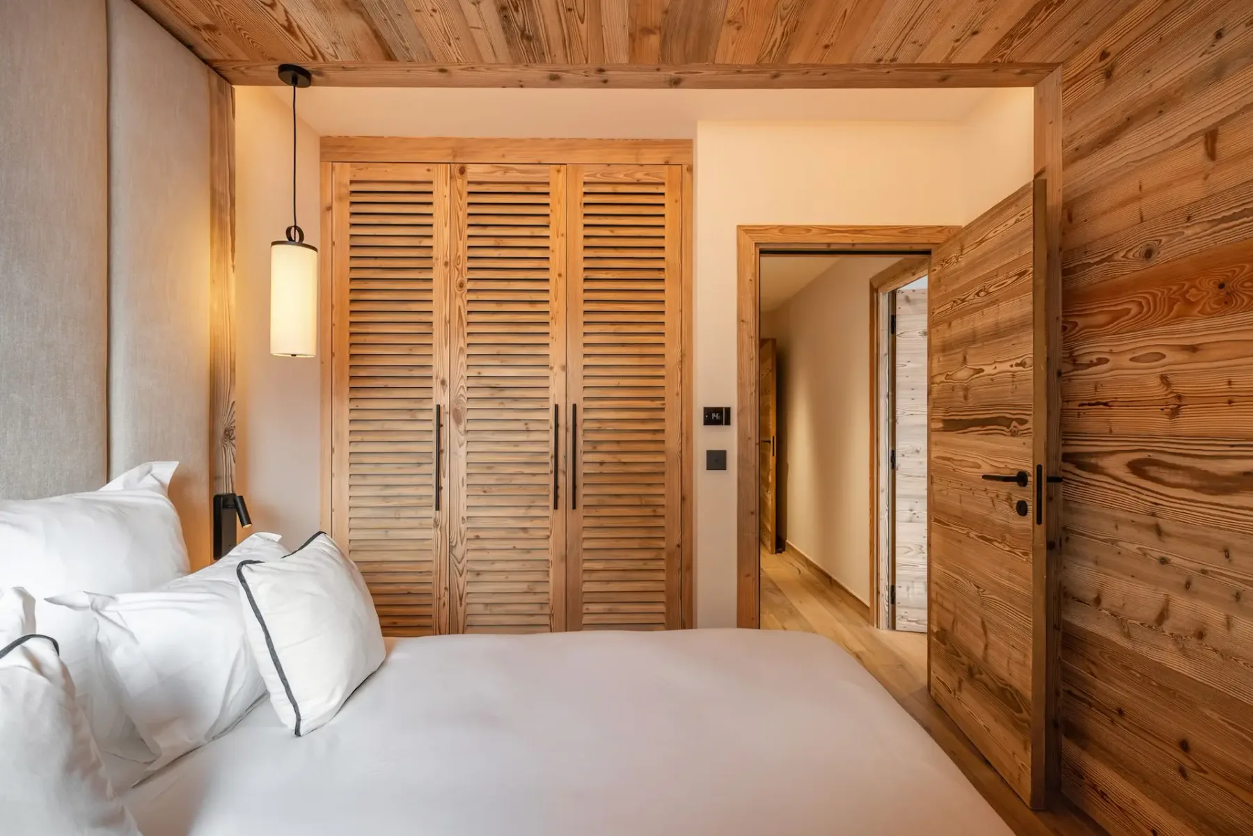 Un dormitorio con una cama blanca, techo de madera y puertas de armario con celosías.
