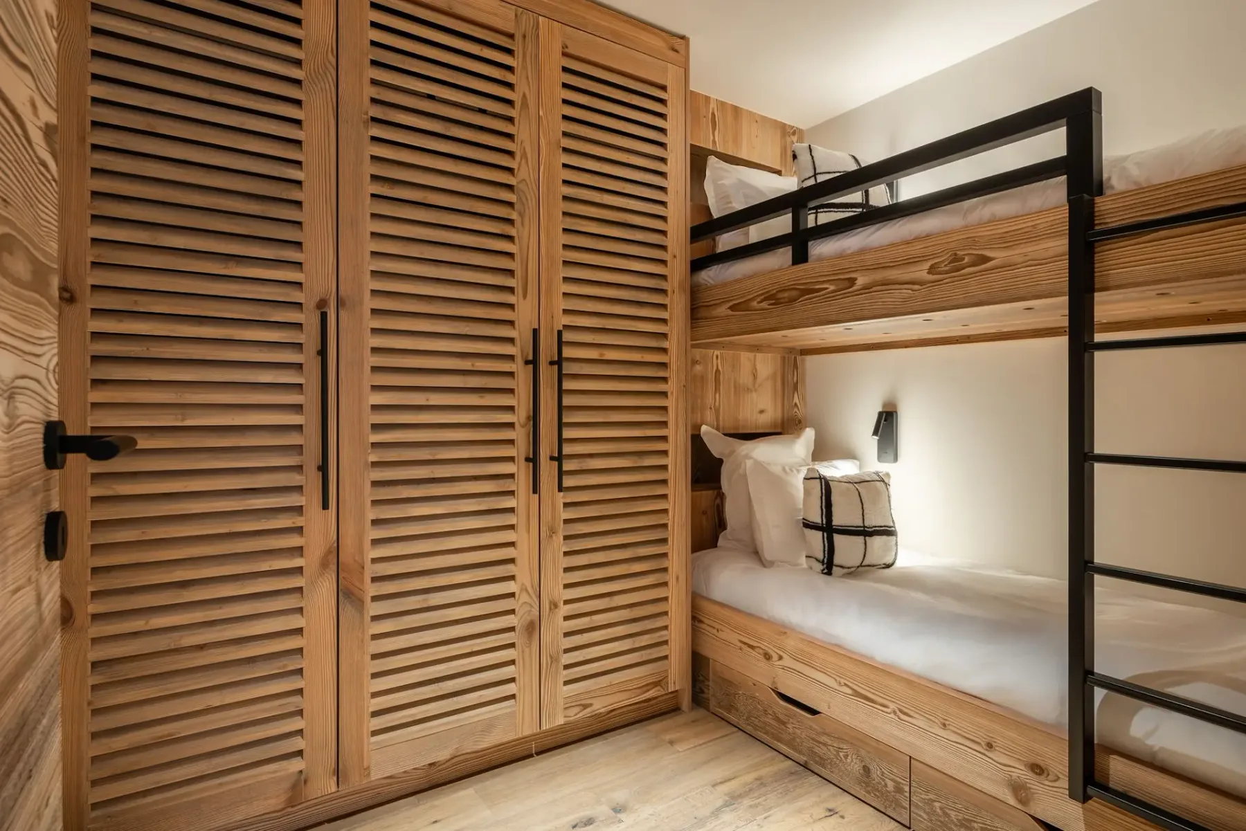 Dormitorio acogedor con literas de madera, un armario con puertas de lamas e iluminación cálida que crea un ambiente acogedor.