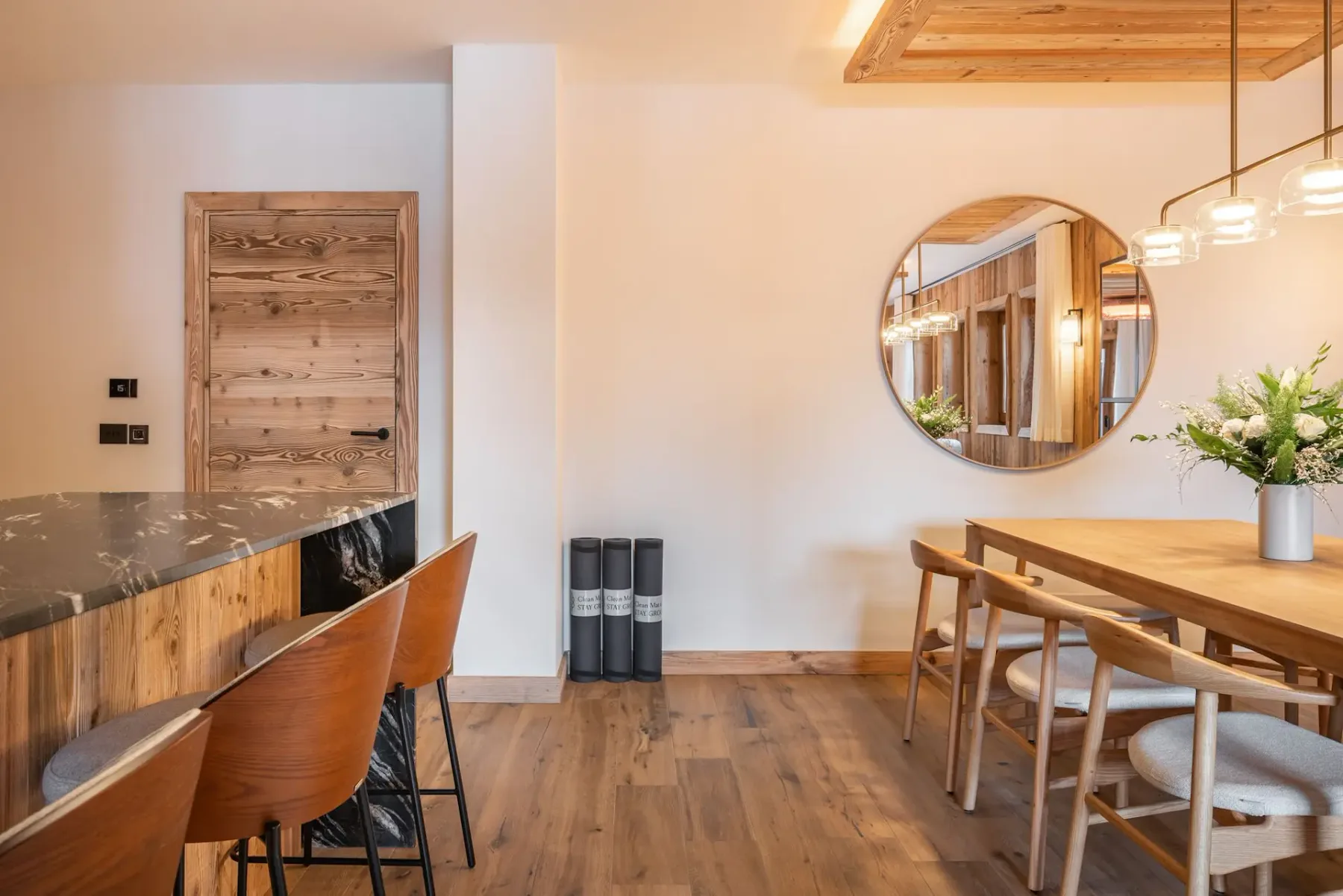 Comedor amueblado en madera con una mesa larga, sillas y un espejo redondo en la pared.