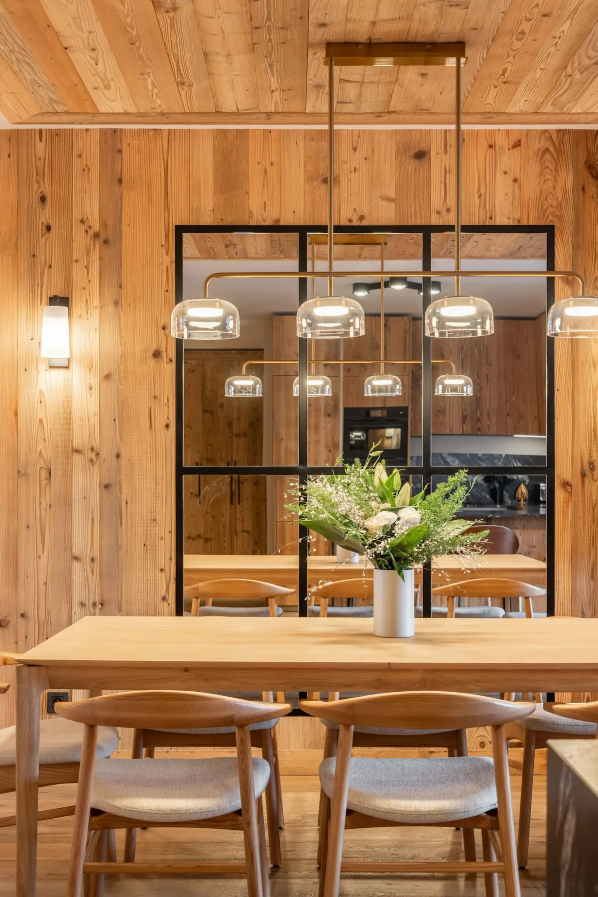 Un comedor de madera cuenta con una mesa larga, sillas y lámparas colgantes.
