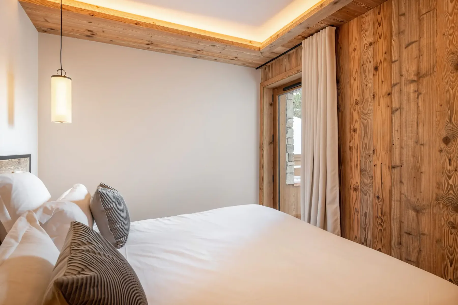 Dormitorio moderno con una mullida cama doble, detalles de madera, iluminación tenue y colores neutros que crean un ambiente cálido y acogedor.