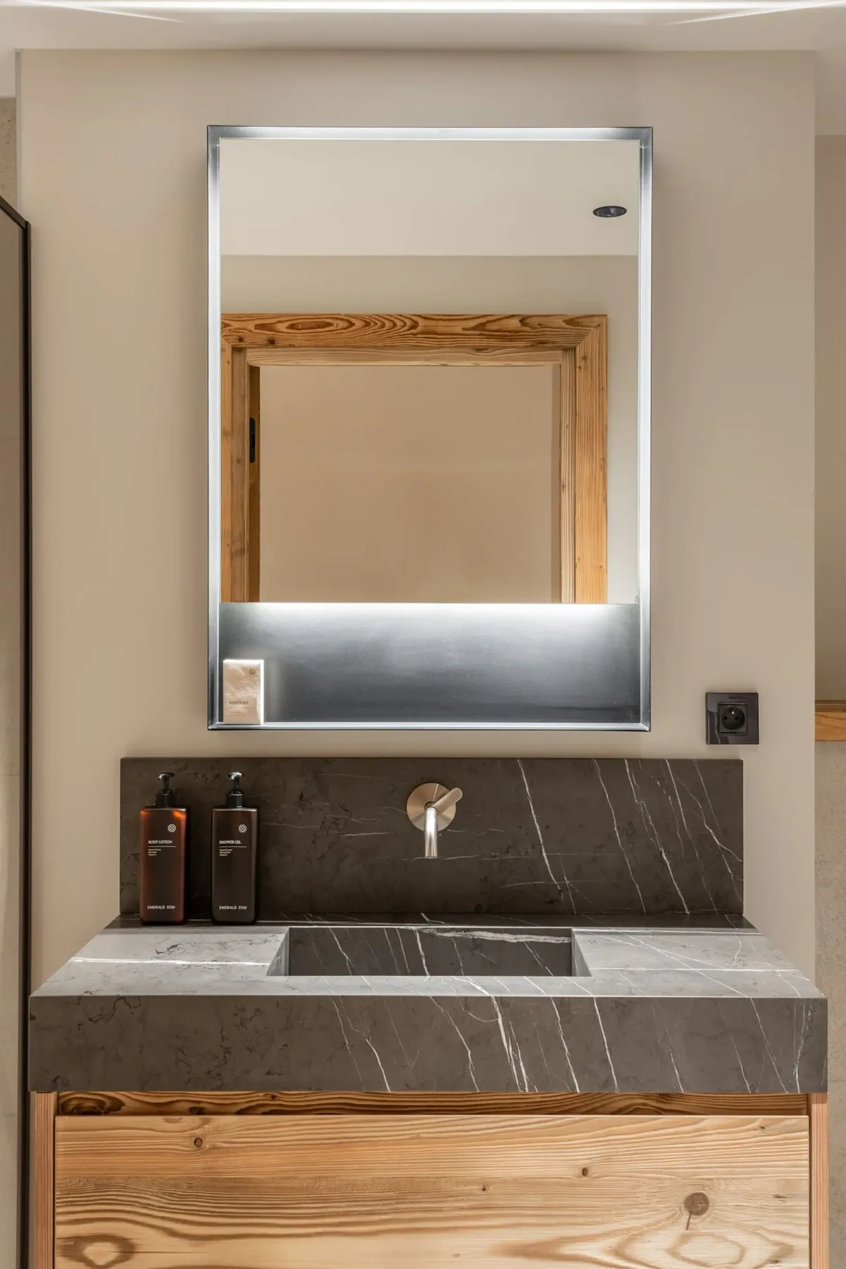 Lavabo de baño con un espejo amplio, salpicadero oscuro y muebles de madera.