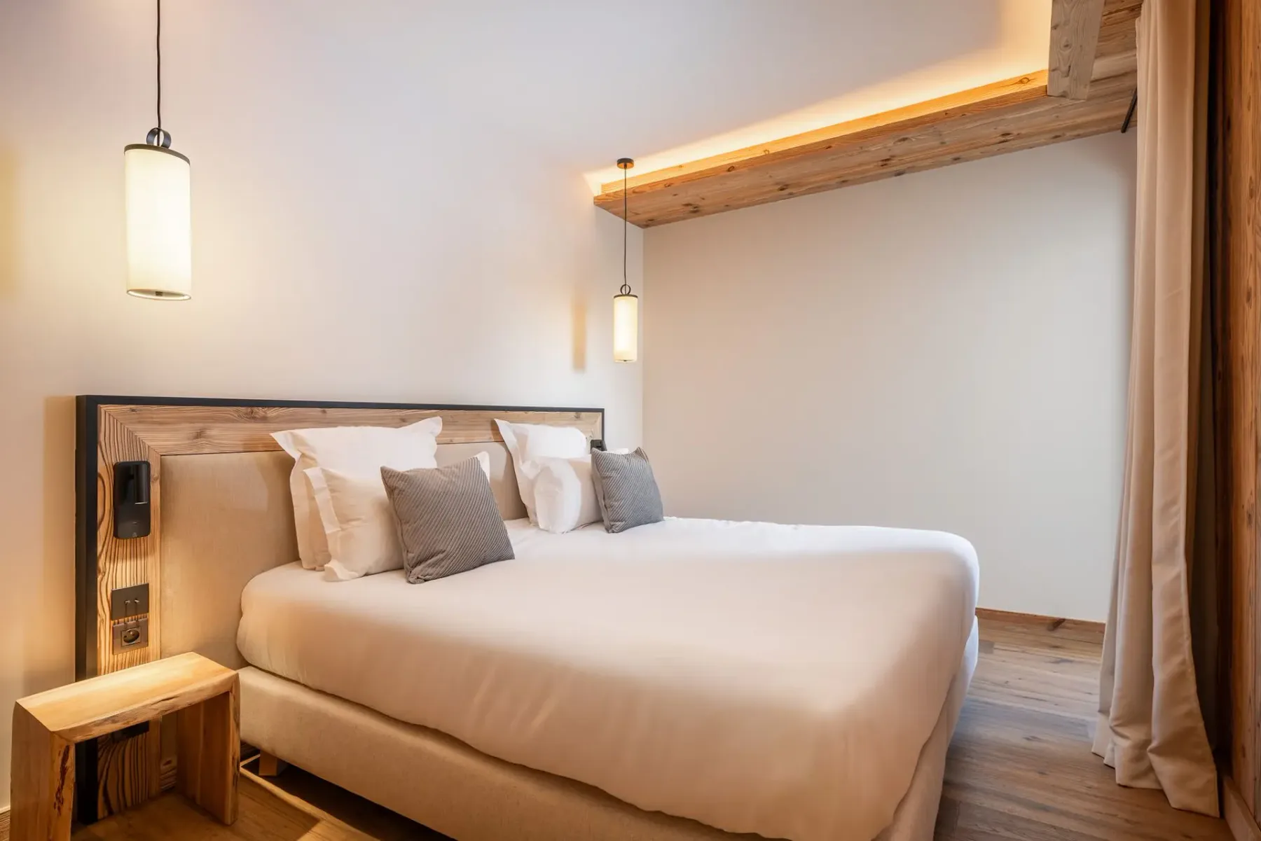 Dormitorio moderno con una mullida cama doble, detalles de madera, iluminación tenue y colores neutros que crean un ambiente cálido y acogedor.