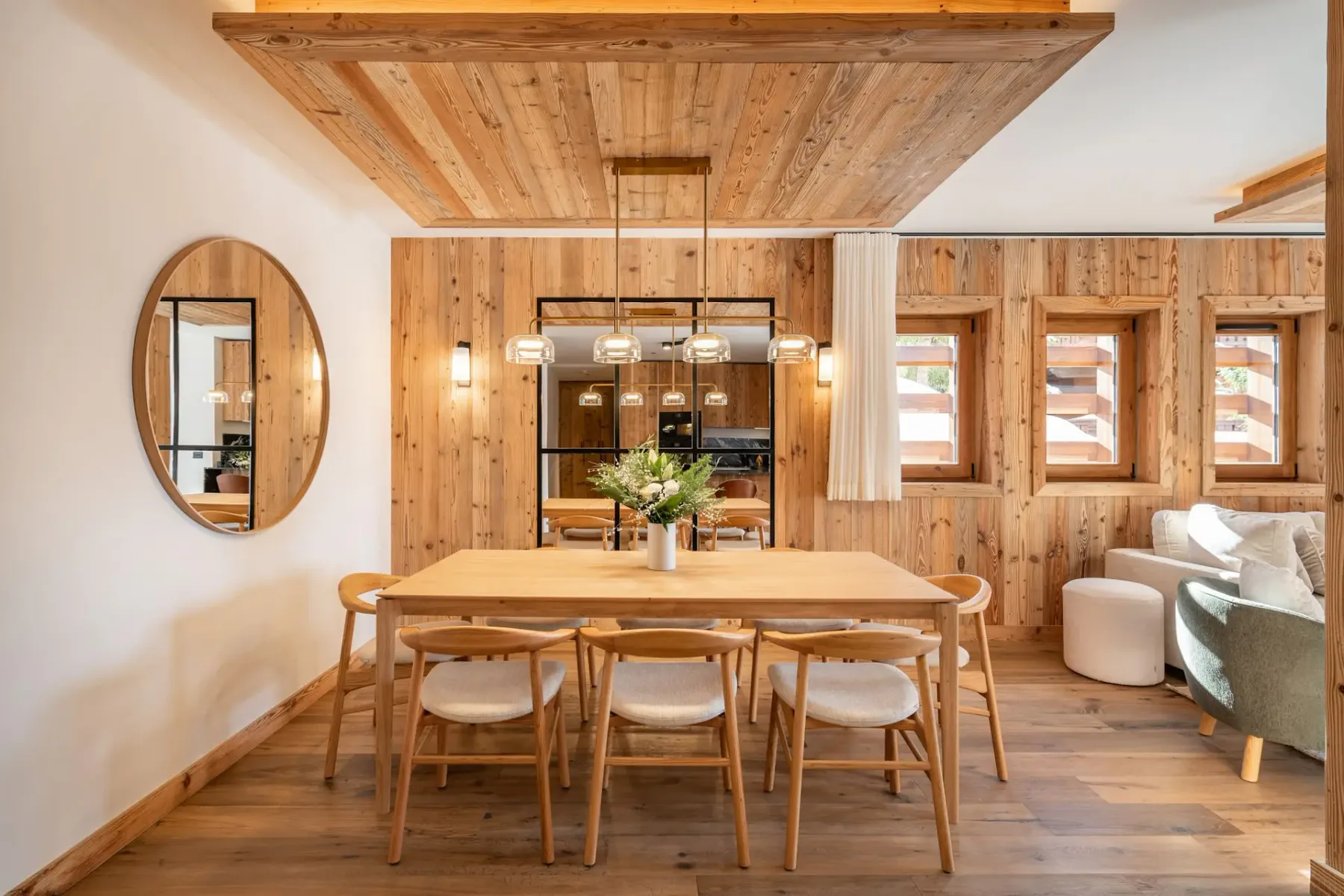 Comedor revestido de madera con una mesa larga y asientos junto a varias ventanas.