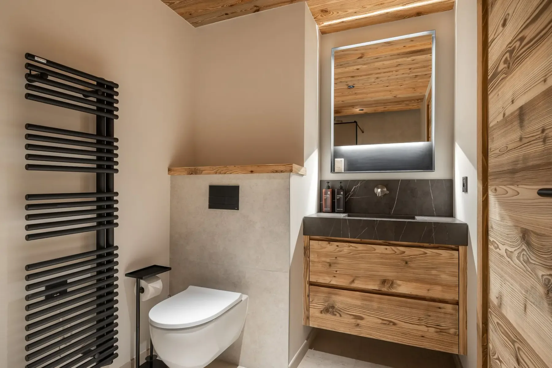 Baño moderno con detalles de madera, un inodoro suspendido, un radiador toallero negro y un mueble de lavabo de madera con espejo.