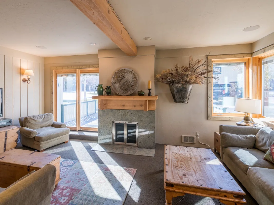 Una sala de estar con chimenea central, asientos y grandes ventanas.