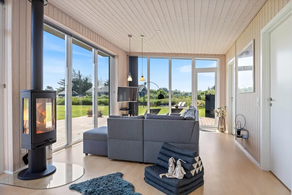 A bright living room with broad windows and a freestanding stove.