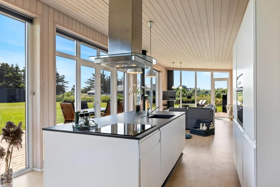 Una cocina y sala de estar diáfanas y luminosas, con grandes ventanas hacia la vegetación.
