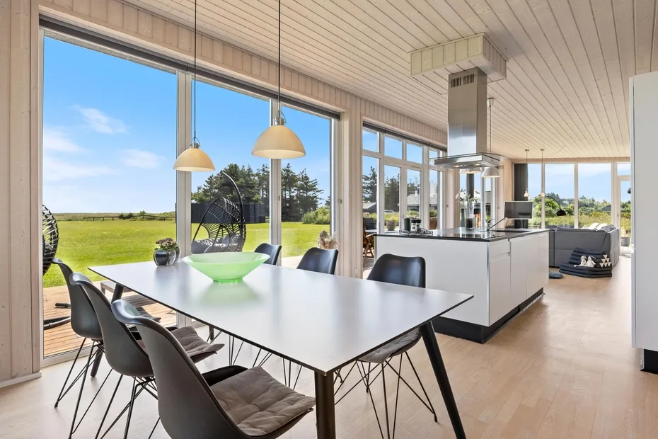 Una luminosa cocina-comedor de concepto abierto con grandes ventanas que dan a un césped.