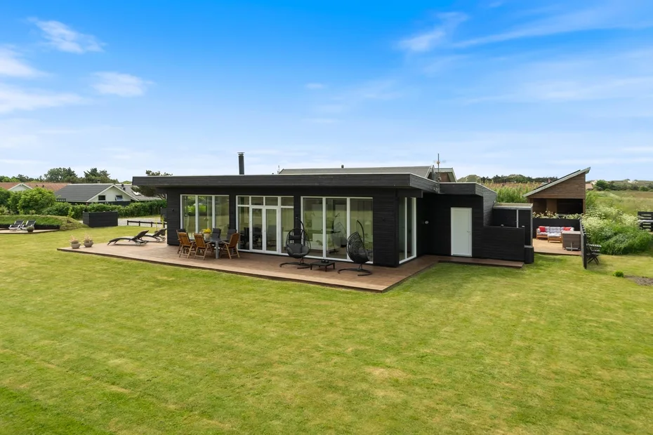 Casa moderna de una planta con un amplio césped y una zona de asientos al aire libre.