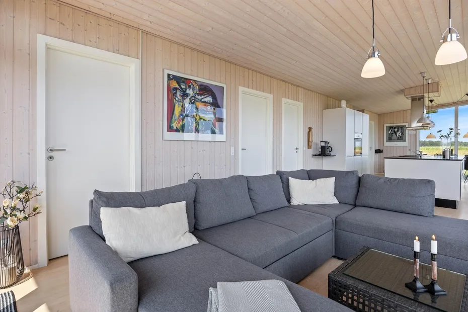 A living room with gray seating, framed artwork, and an open kitchen in the background.