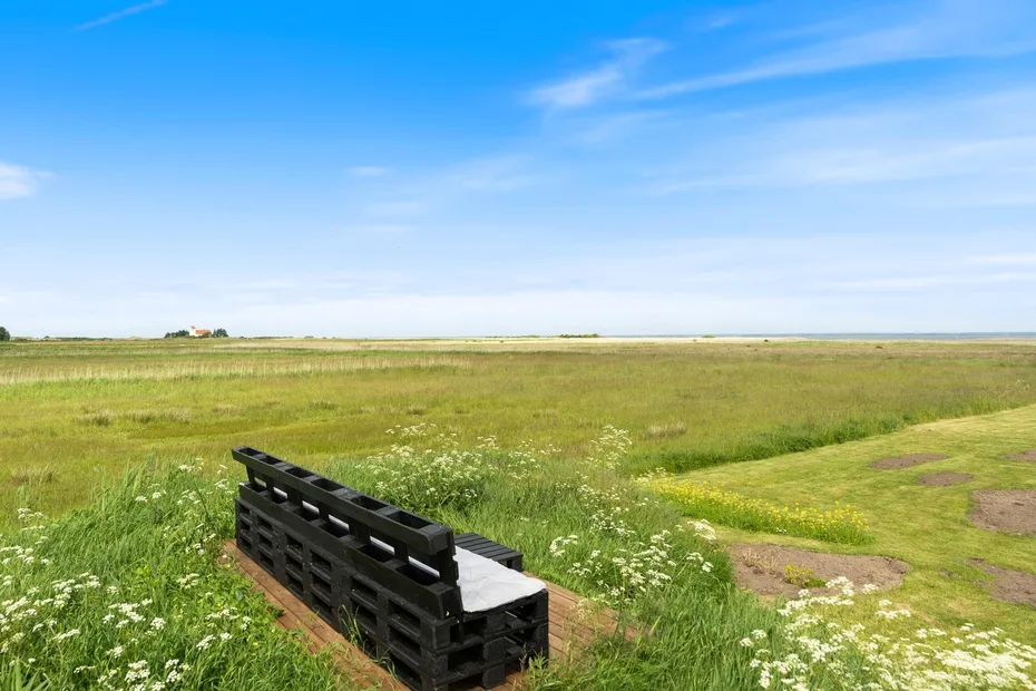 Un banco negro está junto a un amplio campo verde bajo un cielo azul.