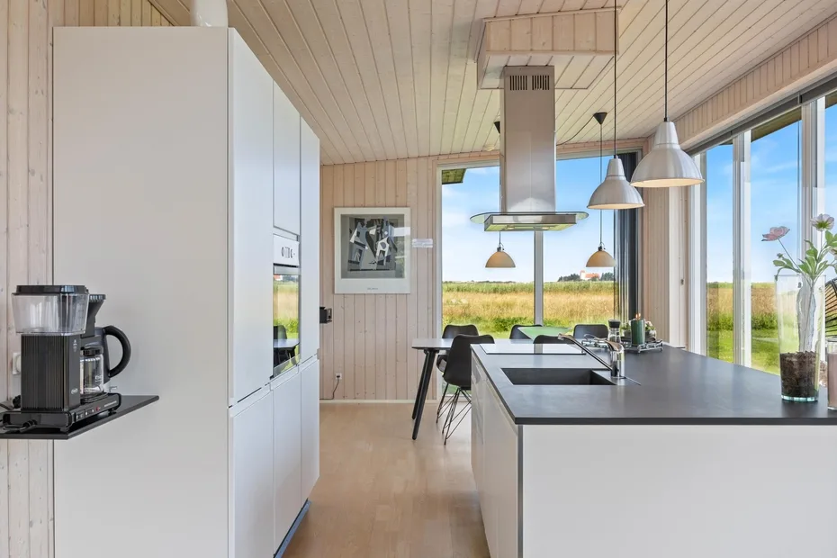 Una cocina luminosa con una isla larga y grandes ventanas con vistas a un paisaje verde.