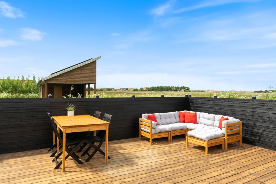 Una terraza de madera con asientos y una mesa de comedor al aire libre da a un paisaje abierto.