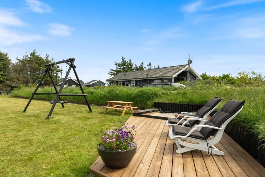 Un césped y una terraza de madera al aire libre, con asientos, un columpio y una mesa de picnic.