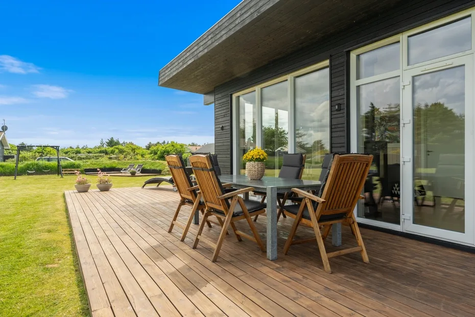 Una terraza de madera junto a una casa moderna tiene asientos al aire libre y puertas de vidrio.