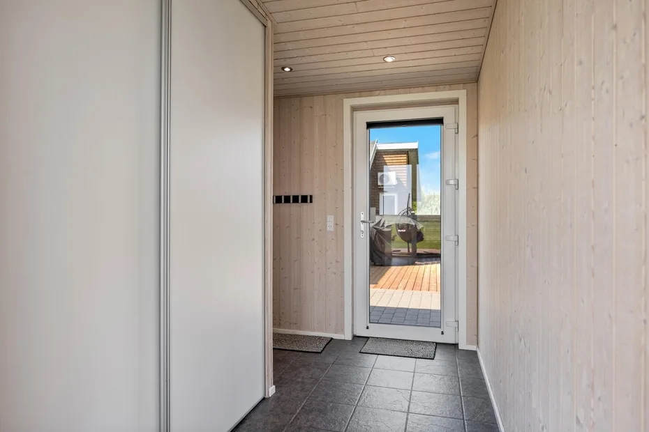 Un estrecho pasillo de entrada con una puerta de cristal que da a una terraza de madera.