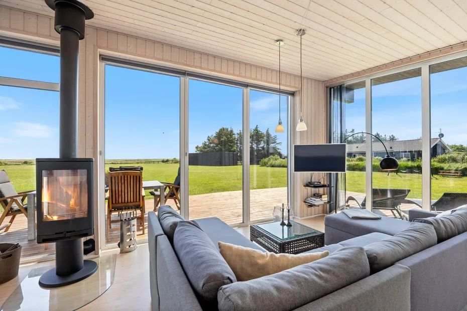 A bright living room with seating, a television, and large windows overlooking a lawn.