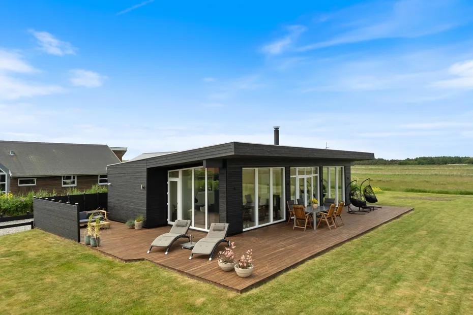 A modern house opens onto a wooden deck with outdoor seating.