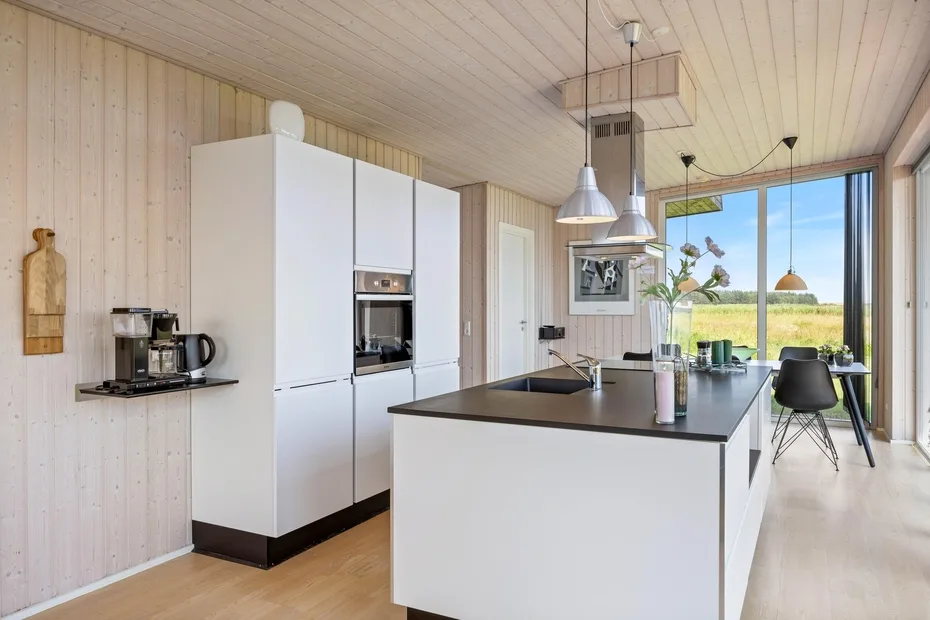 Una cocina luminosa con armarios blancos, una isla central y grandes ventanales.