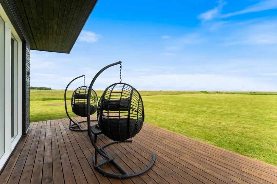 Una terraza de madera con asientos colgantes da a un campo abierto.