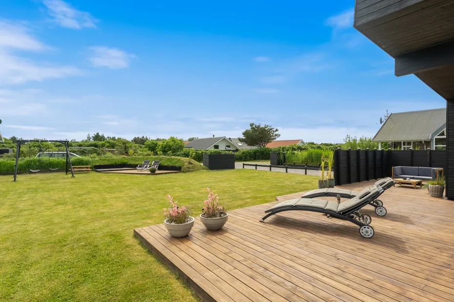 Un patio soleado con una terraza de madera, asientos reclinables y césped amplio.