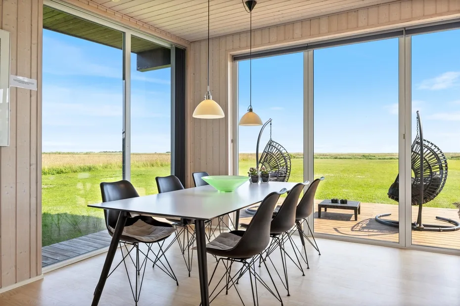 Comedor con mesa y asientos junto a grandes ventanales con vistas a un campo de hierba.