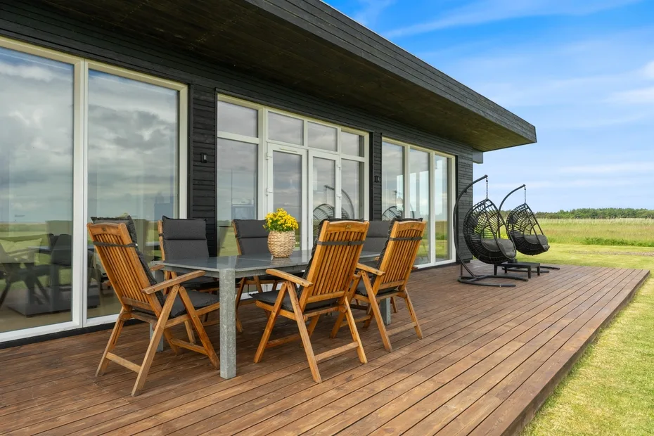 Una terraza de madera amueblada con asientos para comer y sillas colgantes junto a grandes puertas de vidrio.