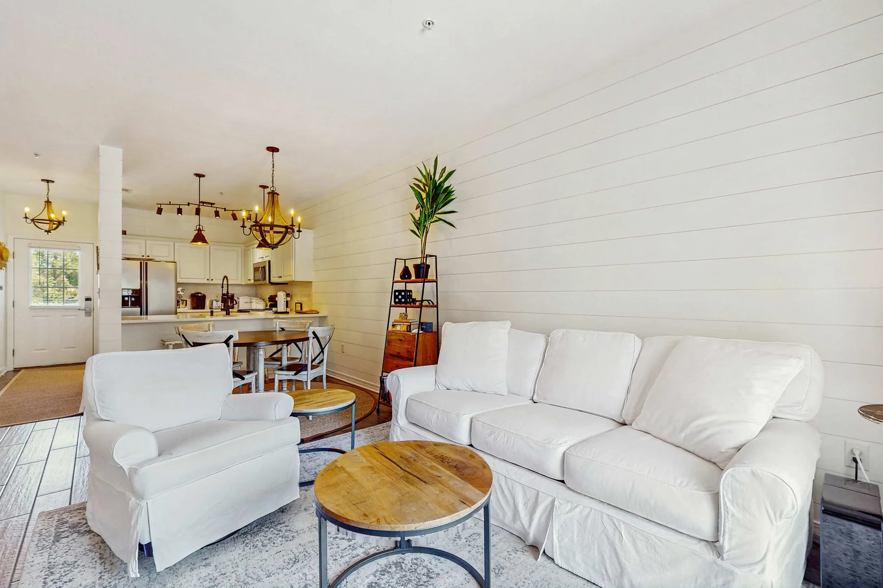 Una sala luminosa con asientos blancos y una cocina abierta al fondo.