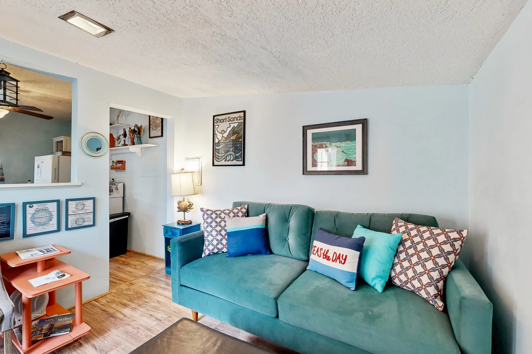 A living room with teal seating and framed artwork on the wall.
