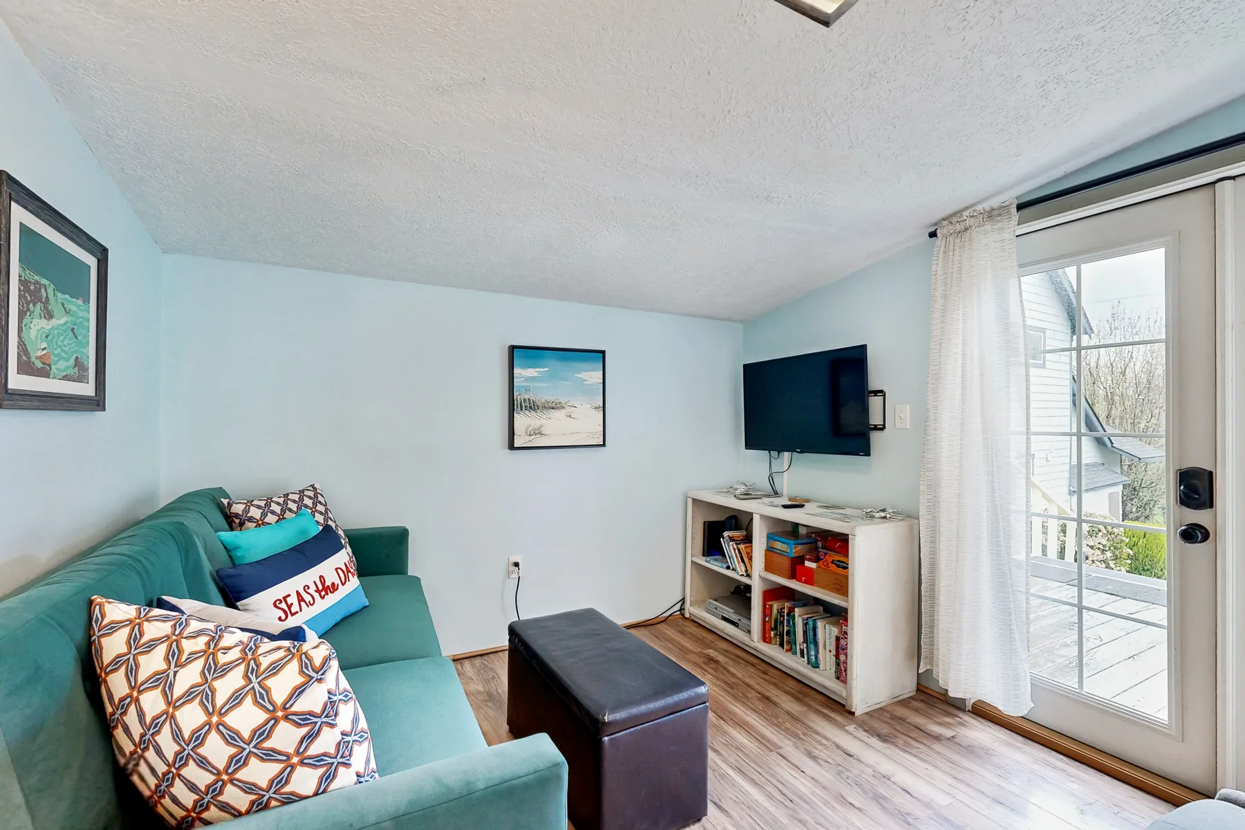 A living room with teal seating, a television, and a glass door to a balcony.