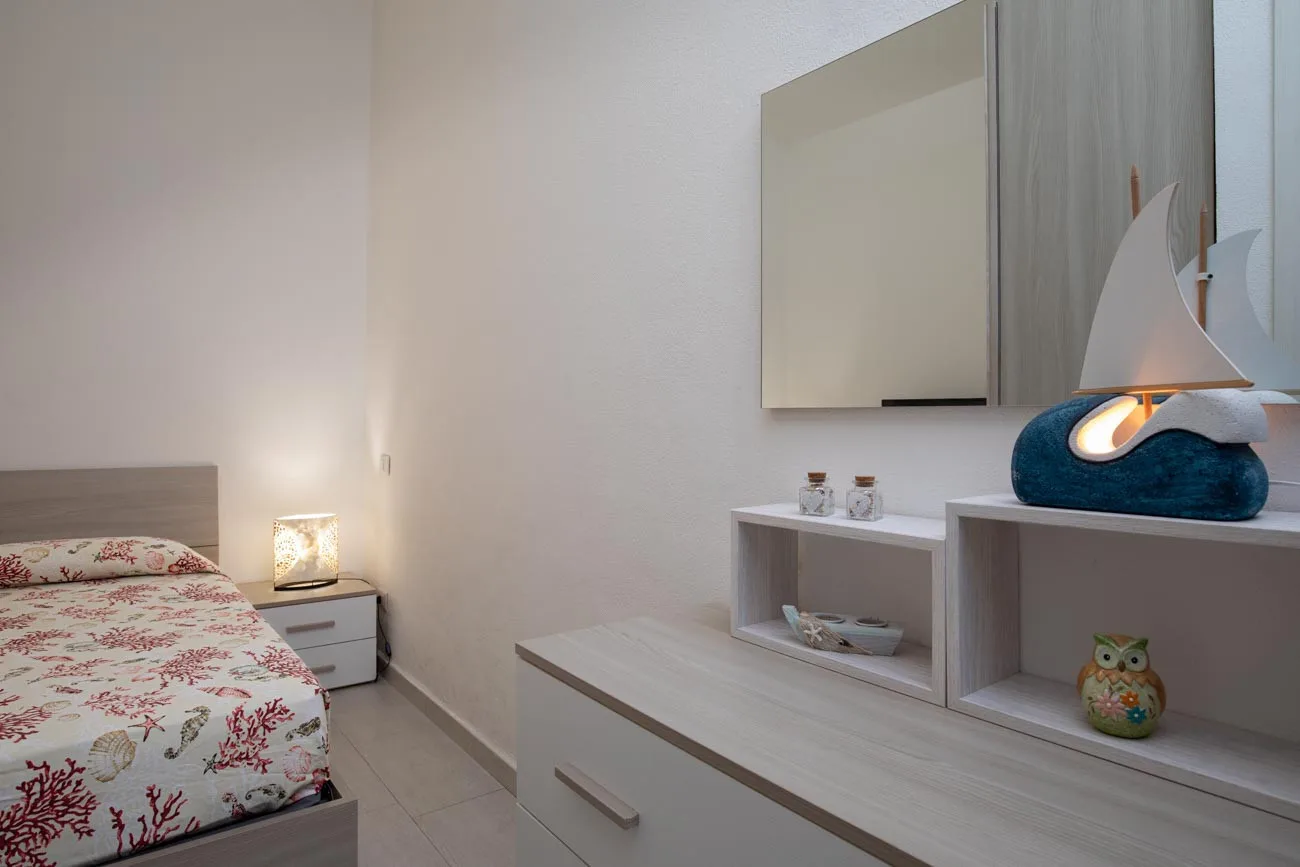 Dormitorio con una colcha floral, una lámpara de noche y muebles de almacenaje claros.