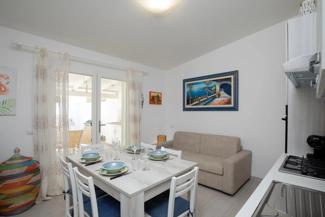 Comedor con una mesa preparada junto a un sofá beige y ventanas luminosas.