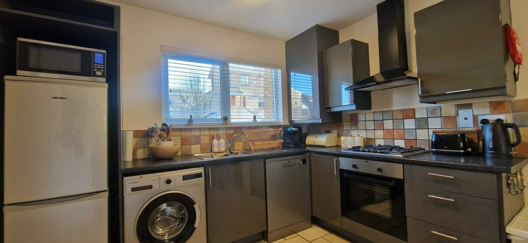 Una cocina con gabinetes oscuros, un refrigerador y electrodomésticos de cocina.