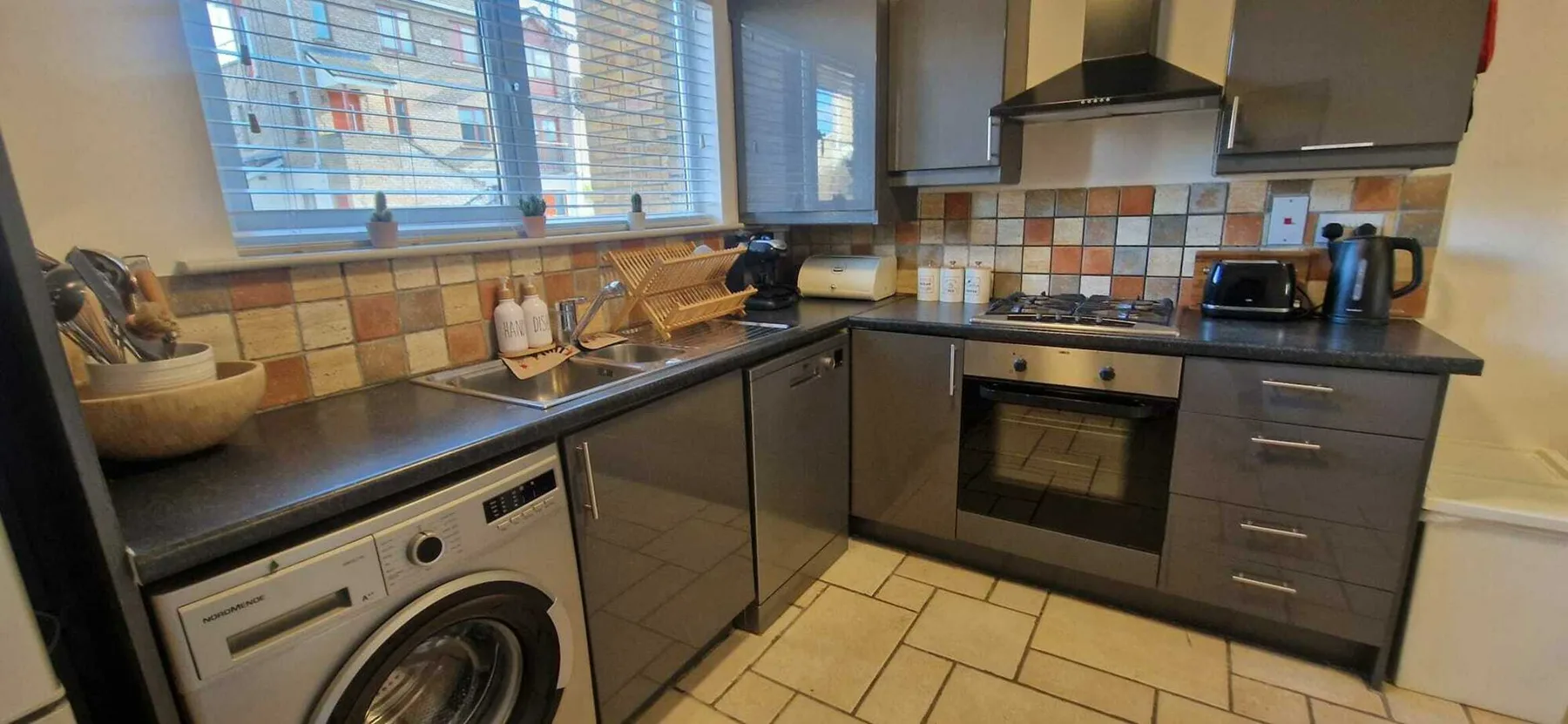Una cocina compacta con gabinetes oscuros, azulejos en la pared y una lavadora.