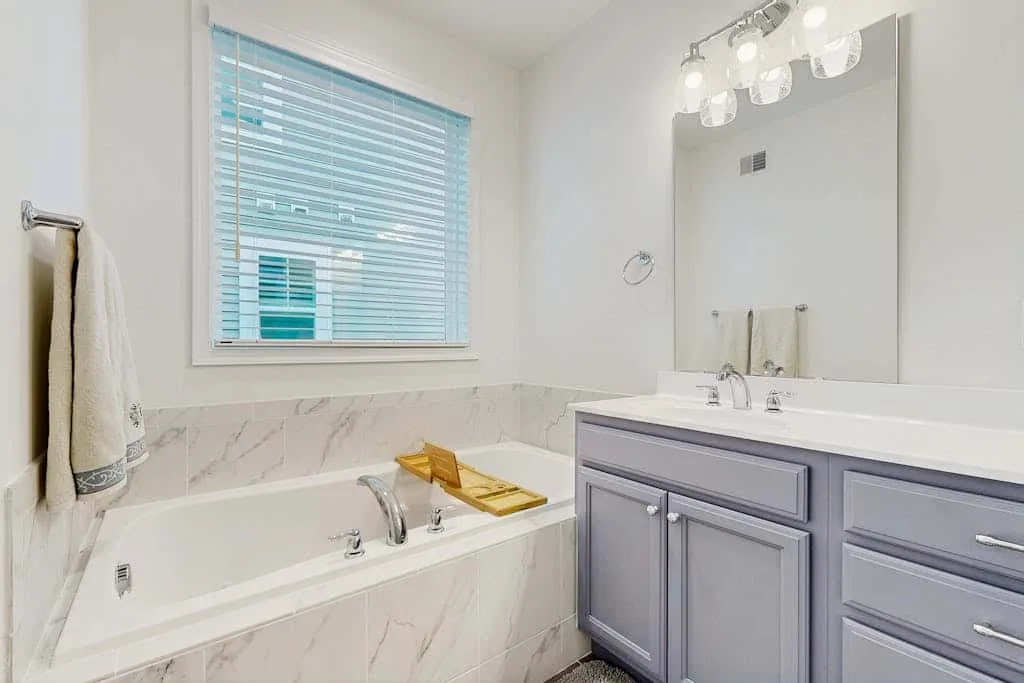 Un baño luminoso con bañera, persianas en la ventana y tocador.